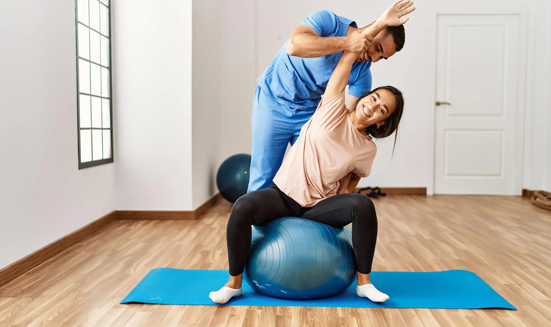 Bewegungstherapie im Reha-Zentrum Felbring &ndash; Physiotherapeut unterst&uuml;tzt Patientin bei Dehn&uuml;bung auf Gymnastikball